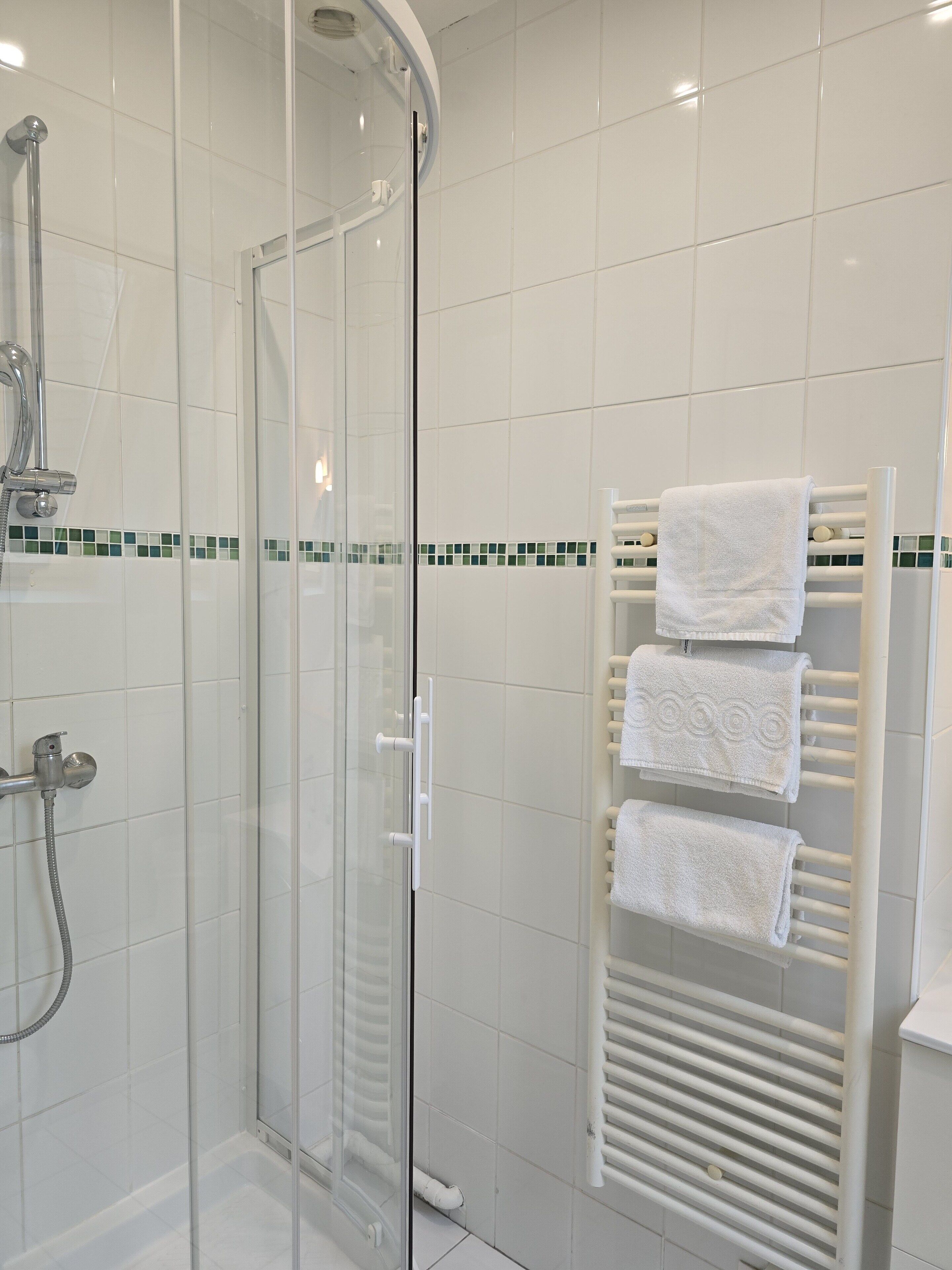 Ein modernes Badezimmer mit einer gläsernen Duschkabine, einem weißen Handtuchhalter und einem gefliesten Boden.