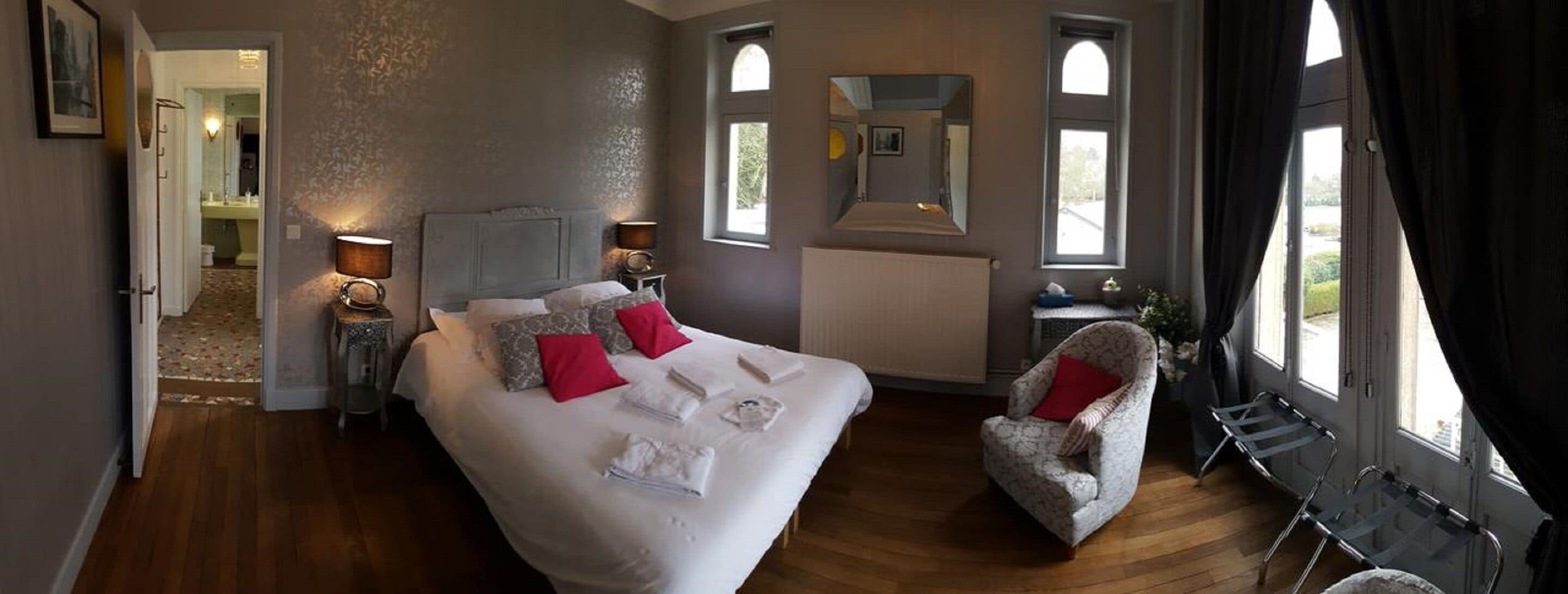 Une chambre d’hôtel avec un grand lit, deux lampes de chevet, une chaise et une vue sur l’extérieur par les fenêtres.