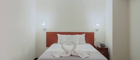 Et hotelværelse med en pænt redt seng, et træhovedgærde, et natbord med en telefon og en flaske samt en vægmonteret lampe.