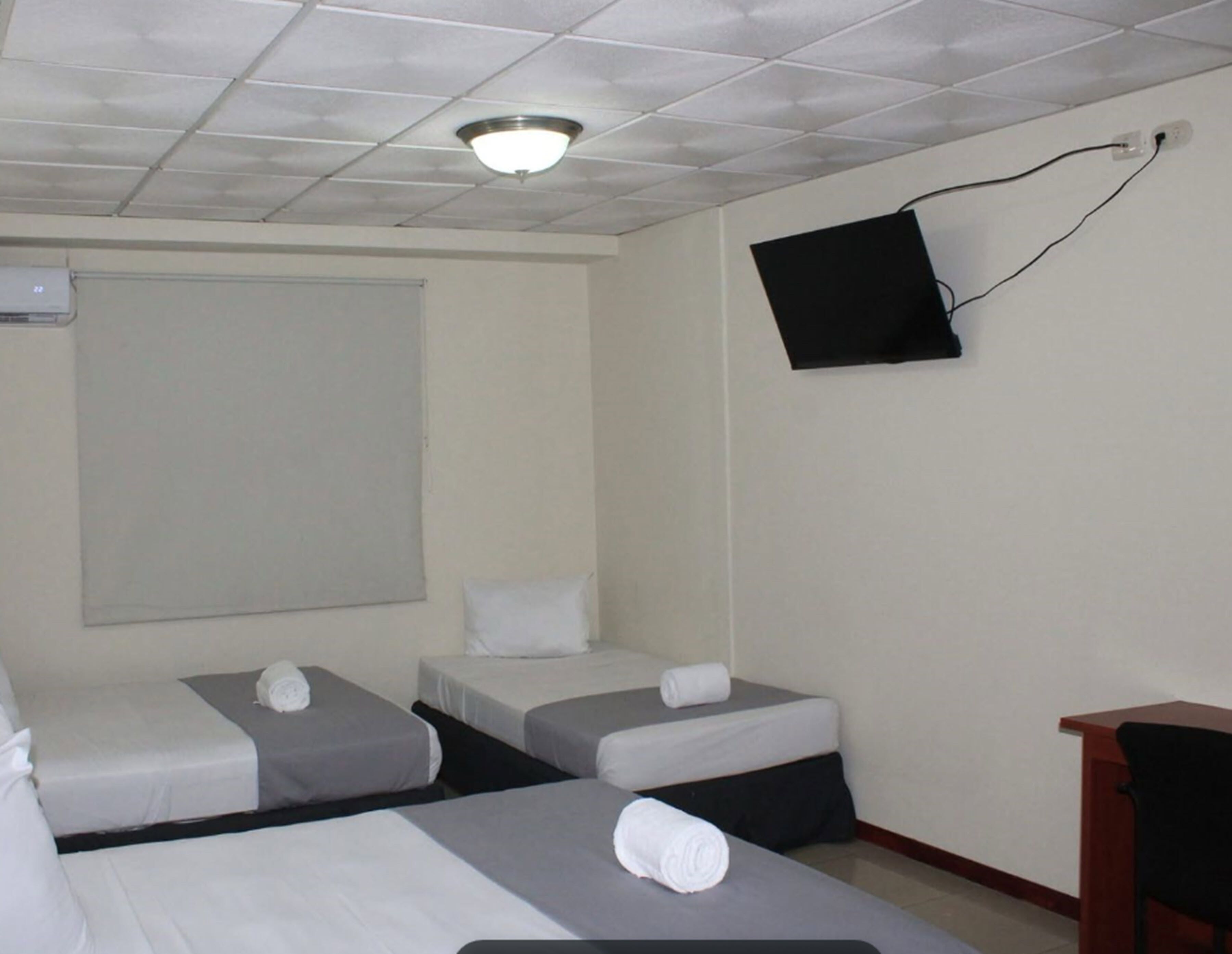 Ein Hotelzimmer mit drei Einzelbetten, einem flachbildfernseher an der Wand und einem Holztisch.