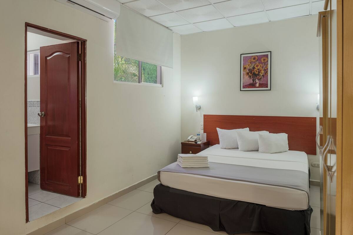 Una habitación de hotel con cama, mesita de noche, un cuadro y una puerta.