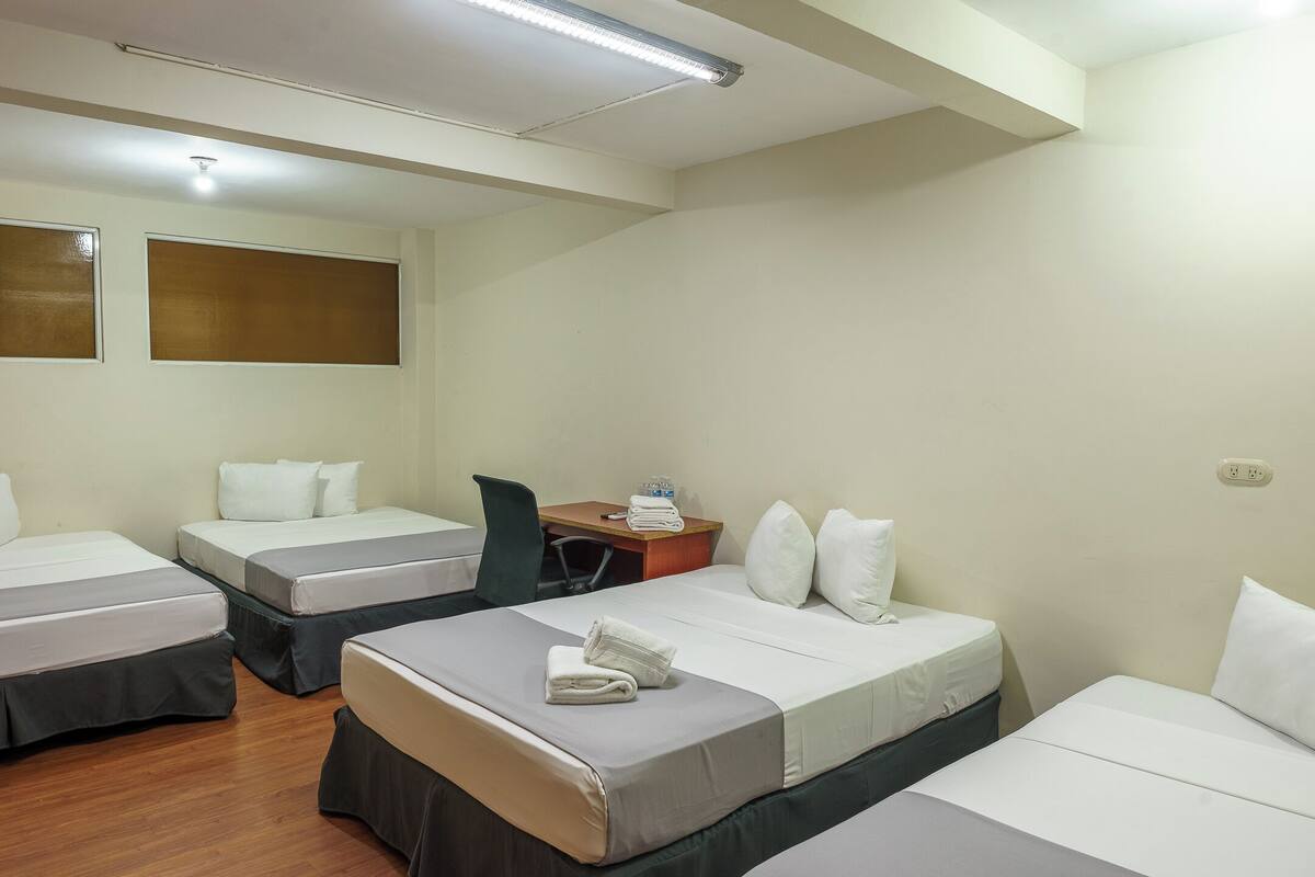 Habitación de hotel con tres camas, un escritorio y una silla.