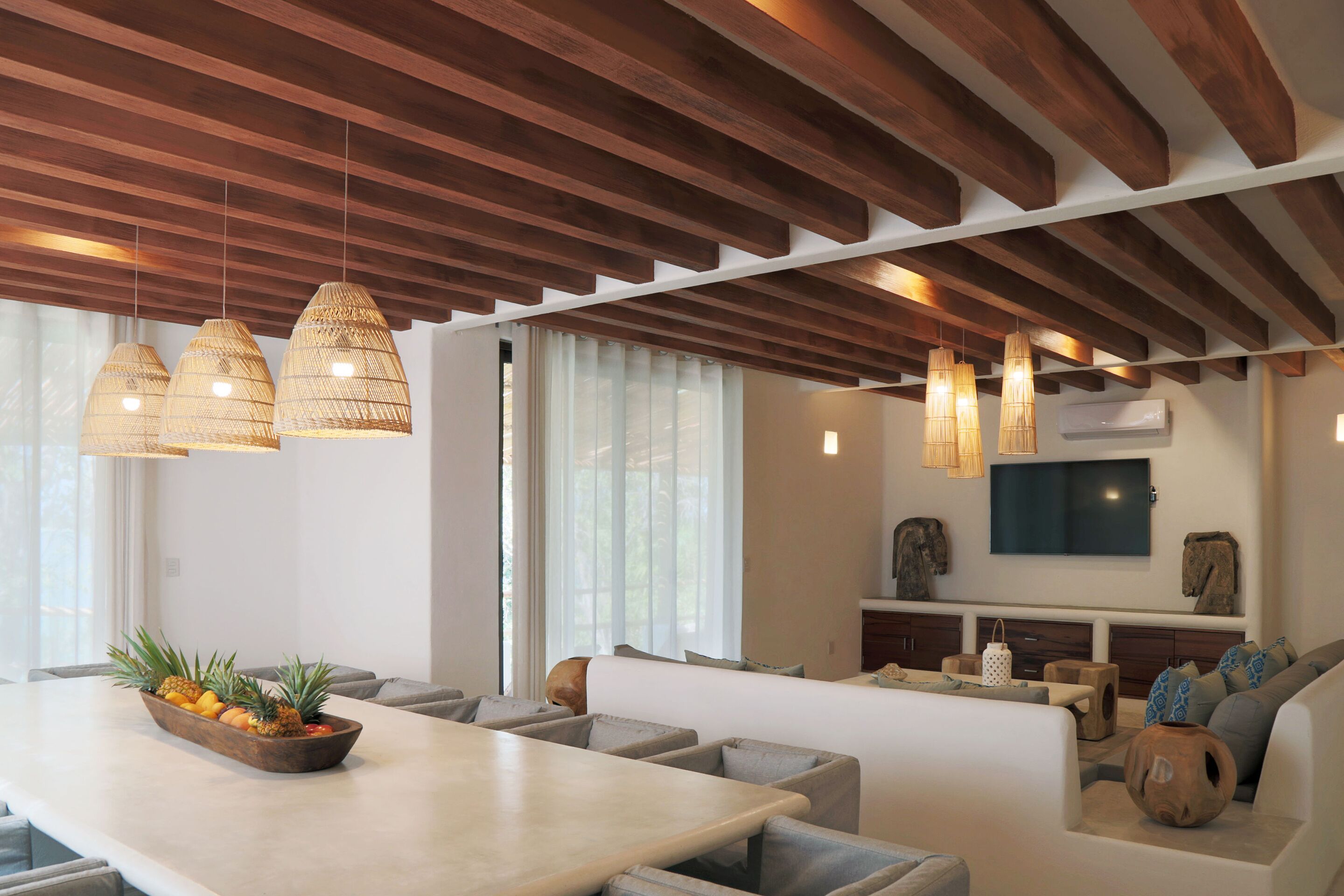 Un salon moderne avec un plafond en bois, un grand téléviseur et un coin salon agrémenté de coussins.