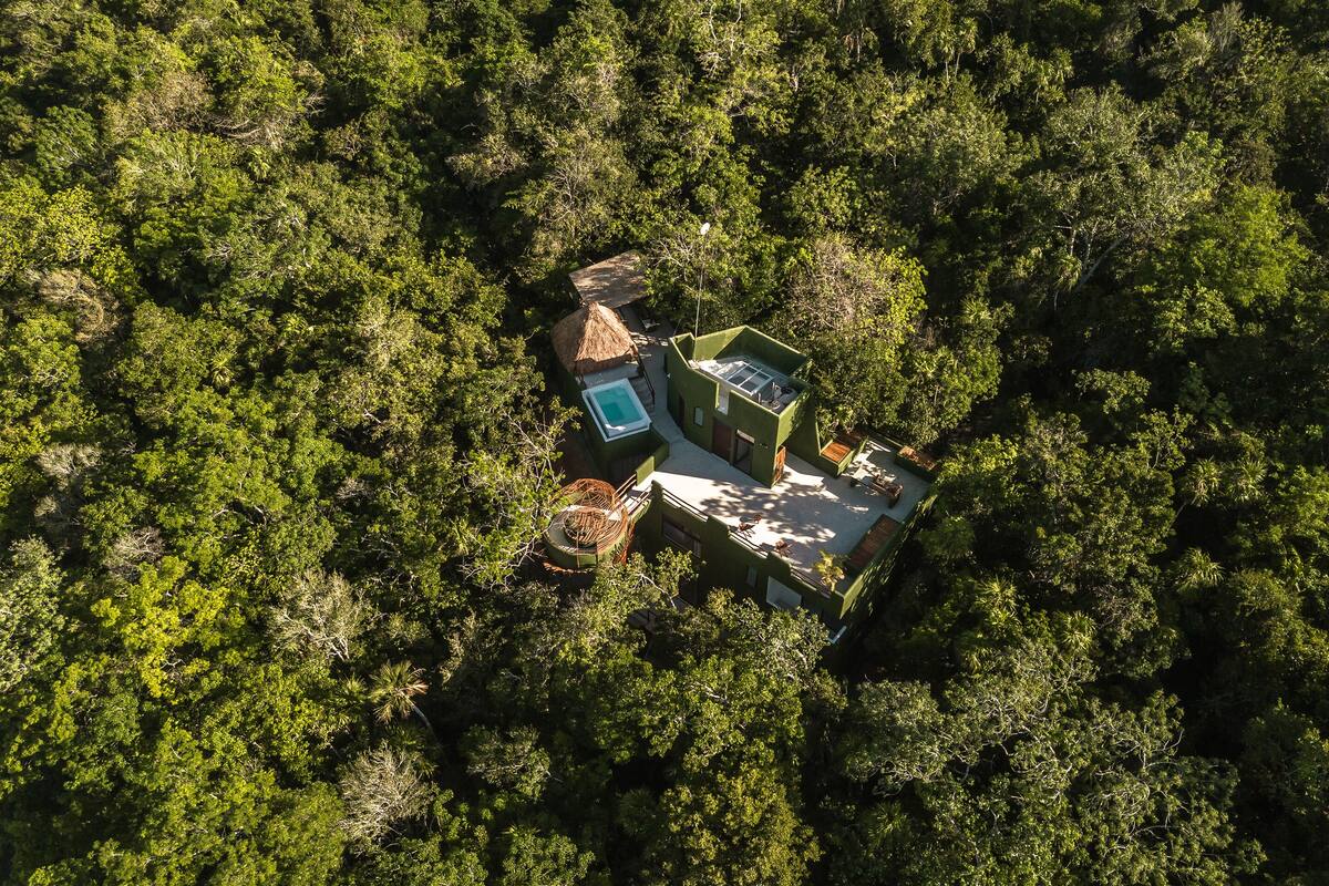 Eine Vogelperspektive zeigt eine abgelegene Öko-Lodge, umgeben von dichtem Wald, mit einem zentralen Gebäude, einem Schwimmbecken und Sitzgelegenheiten im Freien.