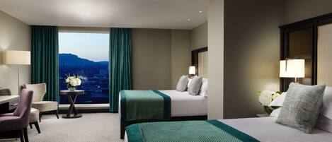A hotel room with a bed, a desk, a chair, a window with curtains, and a view of a cityscape.