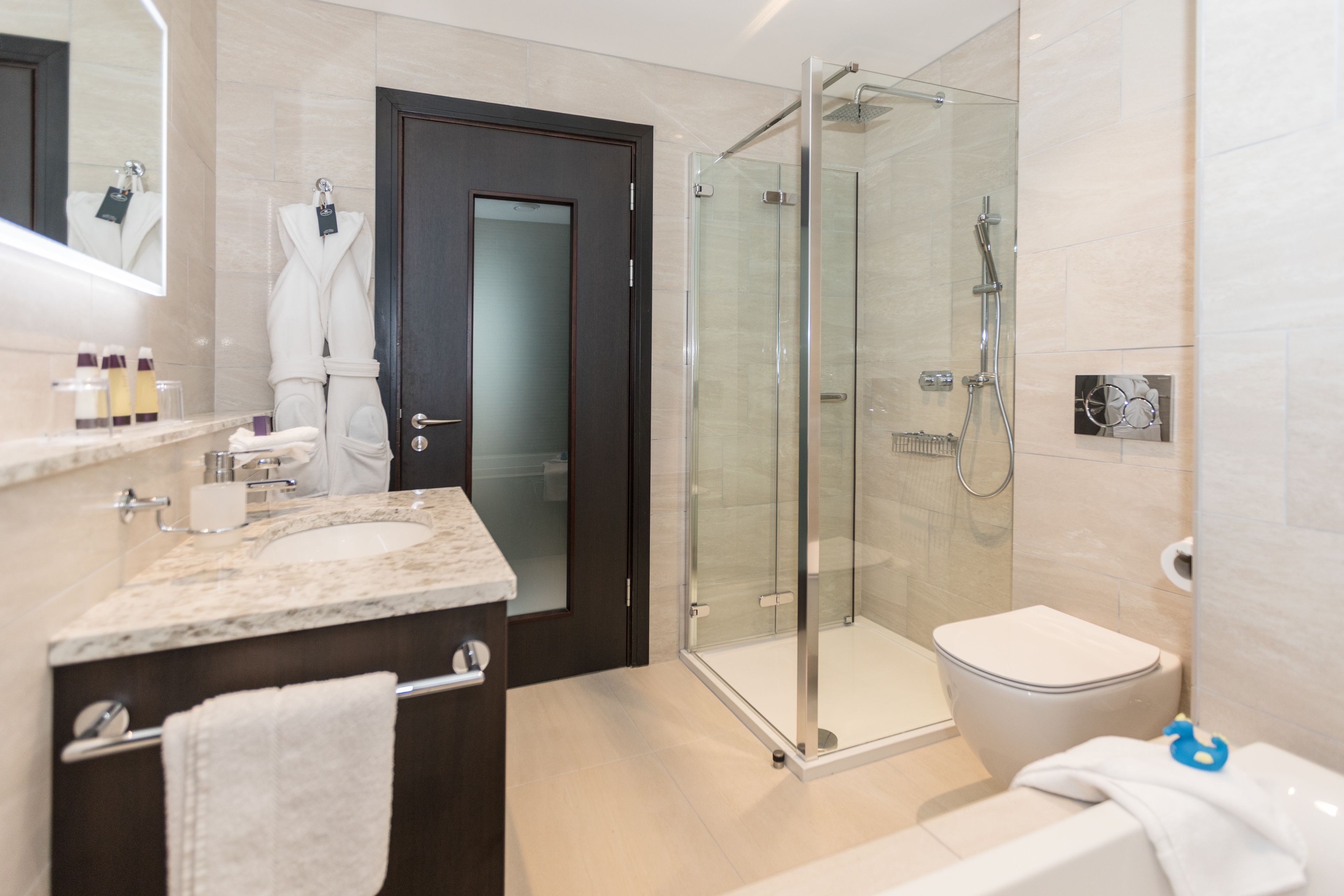A modern bathroom with a glass-enclosed shower, a separate toilet, and a vanity with a marble countertop.