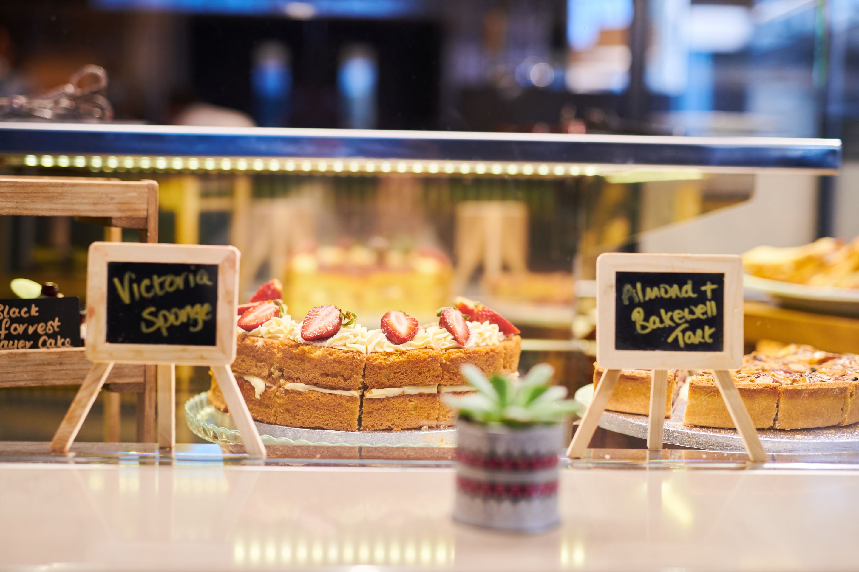 Eine Vitrine mit Kuchen, auf denen 'Victoria Sponge' und 'Mandel-Bakewell-Tarte' steht.