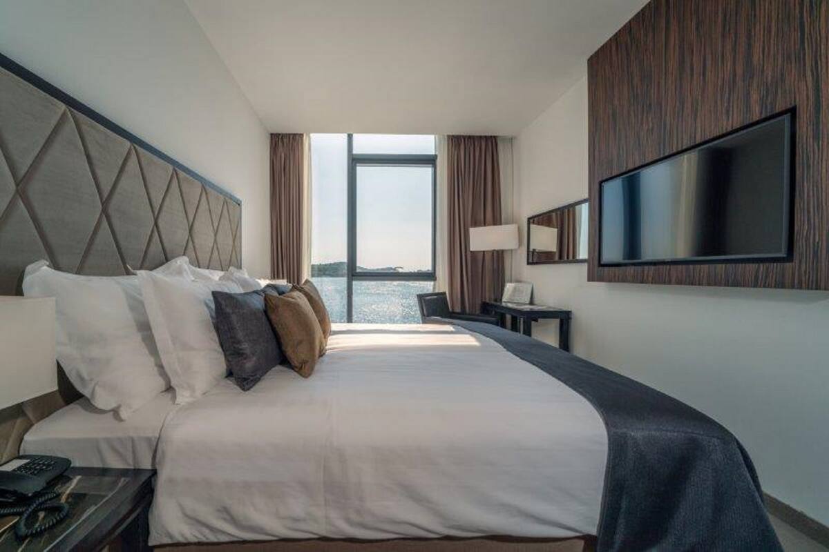 Une chambre d’hôtel dotée d’un grand lit, d’un téléviseur à écran plat fixé au mur, d’un bureau avec une lampe et offrant une vue sur l’eau.