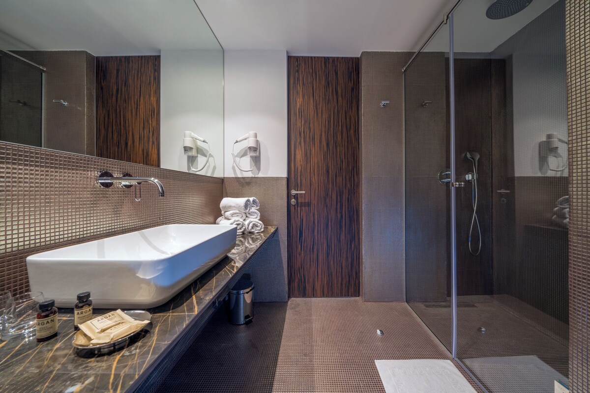 A modern bathroom with a large sink, a glass shower enclosure, and a wooden vanity.