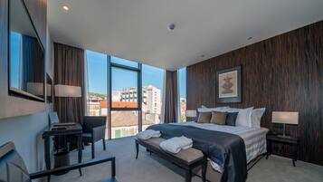 Una habitación de hotel moderna con una cama grande, un escritorio, una silla y vistas a la ciudad.