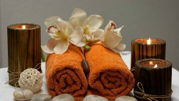 Un entorno de spa con toallas naranjas enrolladas, flores blancas, velas y piedras lisas.