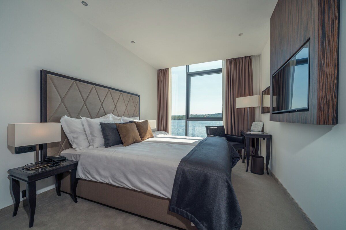 Une chambre d’hôtel moderne dotée d’un grand lit, d’un bureau, d’une chaise, d’une télévision et offrant une vue sur l’eau.