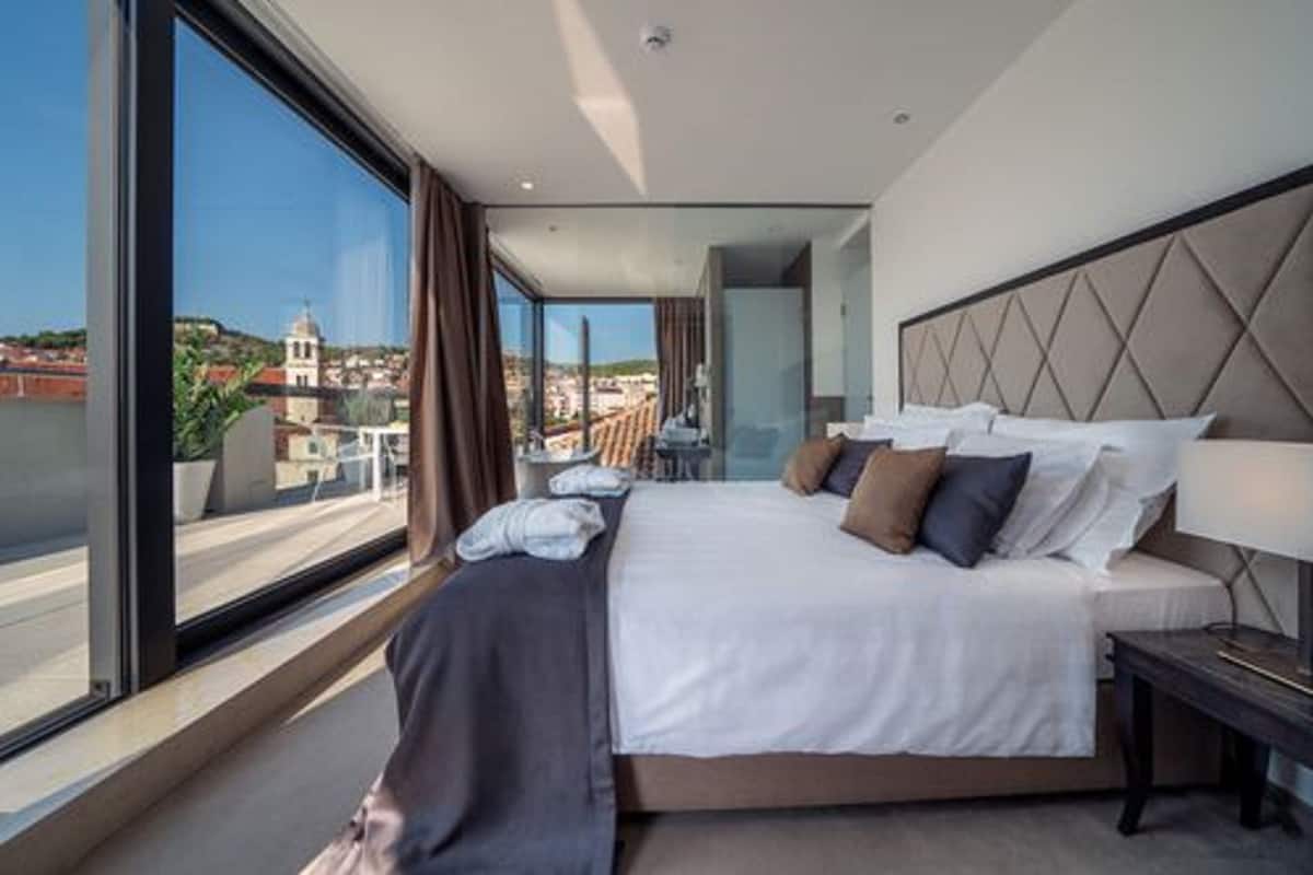 Une chambre d’hôtel moderne, dotée d’un grand lit, offrant une vue sur la ville et permettant d’admirer le paysage urbain à travers la fenêtre.