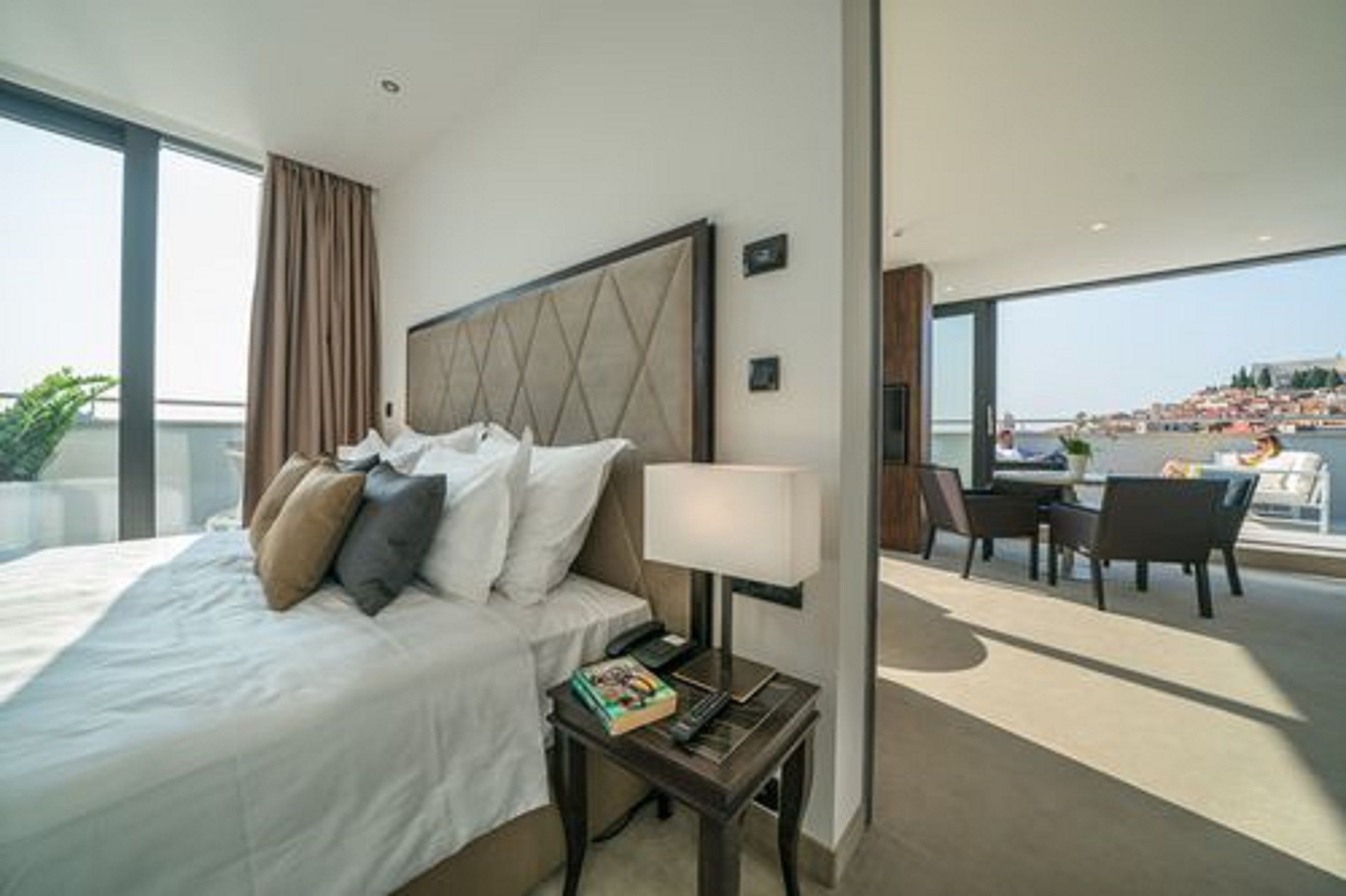 Habitación de hotel con una cama, una mesita de noche con lámpara y vistas a la ciudad.