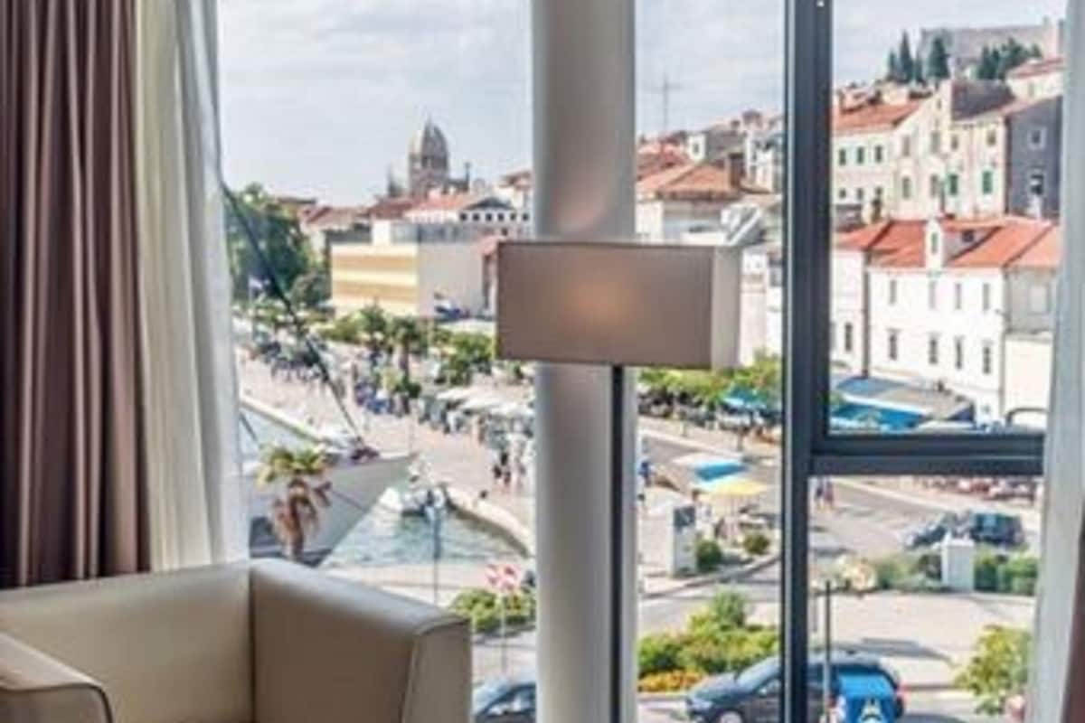 Une chambre d’hôtel avec une grande fenêtre, un canapé, un lit et une lampe.