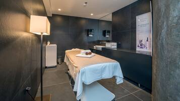 A modern spa room with a massage table, a small sink, and a mirror.