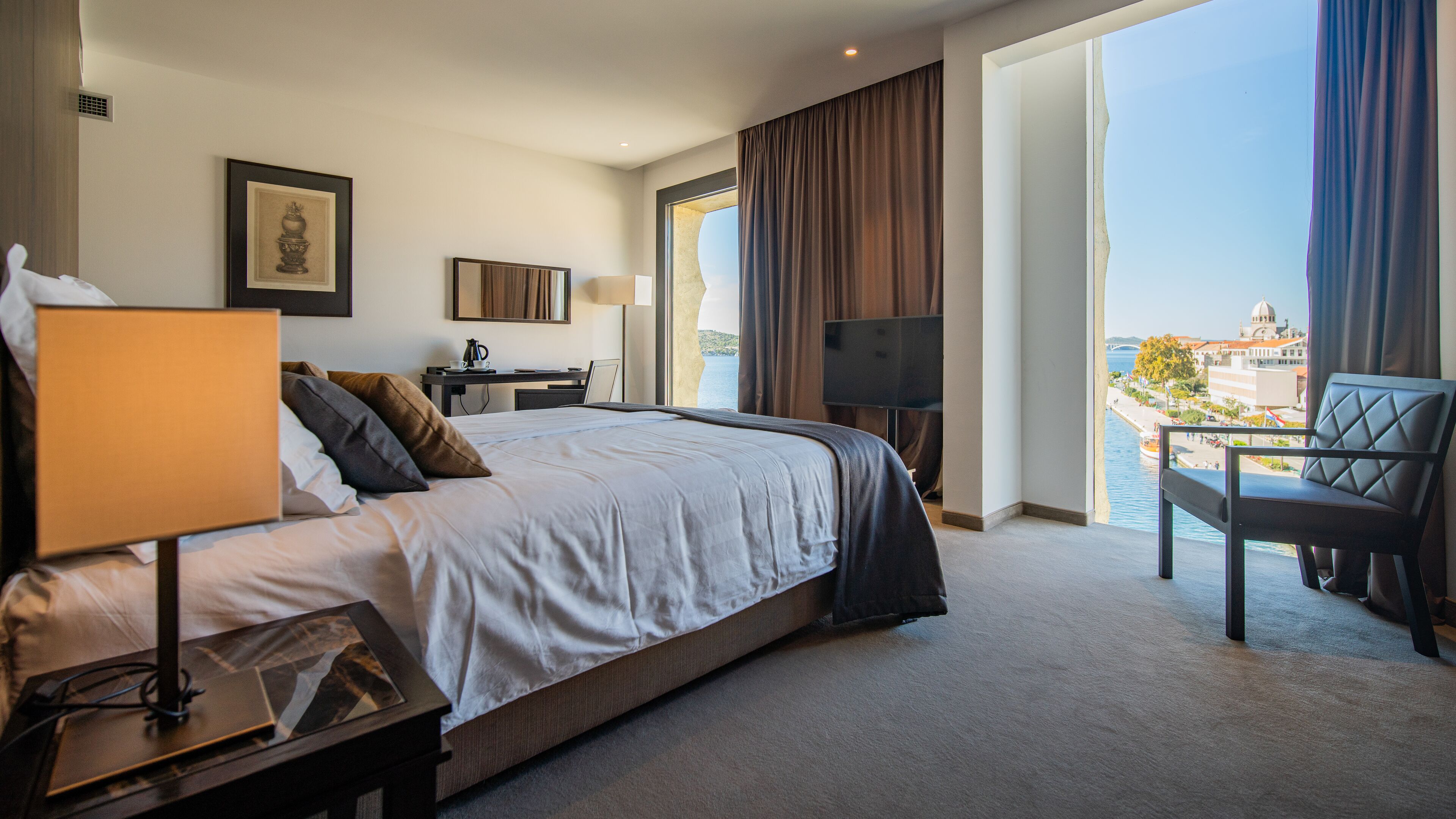 Une chambre d’hôtel avec un grand lit, un bureau, une chaise, une télévision et un balcon offrant une vue sur la ville.