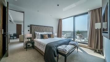 A modern hotel room with a large bed, a bedside table with a lamp, a view of the balcony, and a chair.