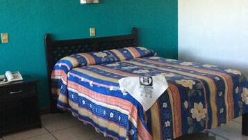 A bed in a room with teal walls, a patterned bedspread, and a white towel with a logo on it.