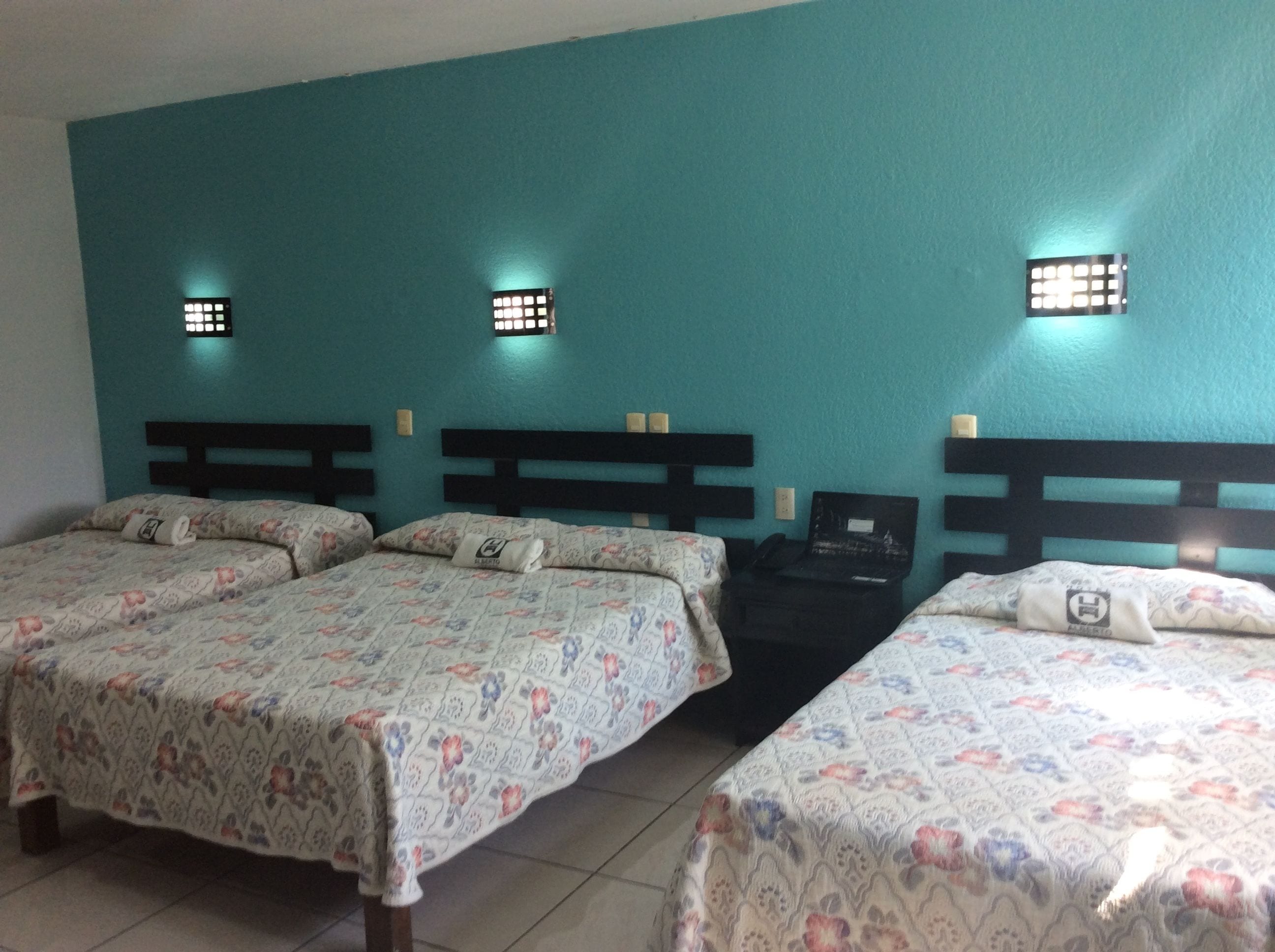 A hotel room with two beds, teal walls, and small wall-mounted lights.