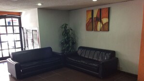 Eine Sitzecke mit zwei schwarzen Sofas, einem Blumentopf und einer Wand mit abstrakter Kunst.