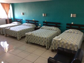 Ein Hotelzimmer mit drei Betten, gefliestem Boden und einer türkisblauen Wand.