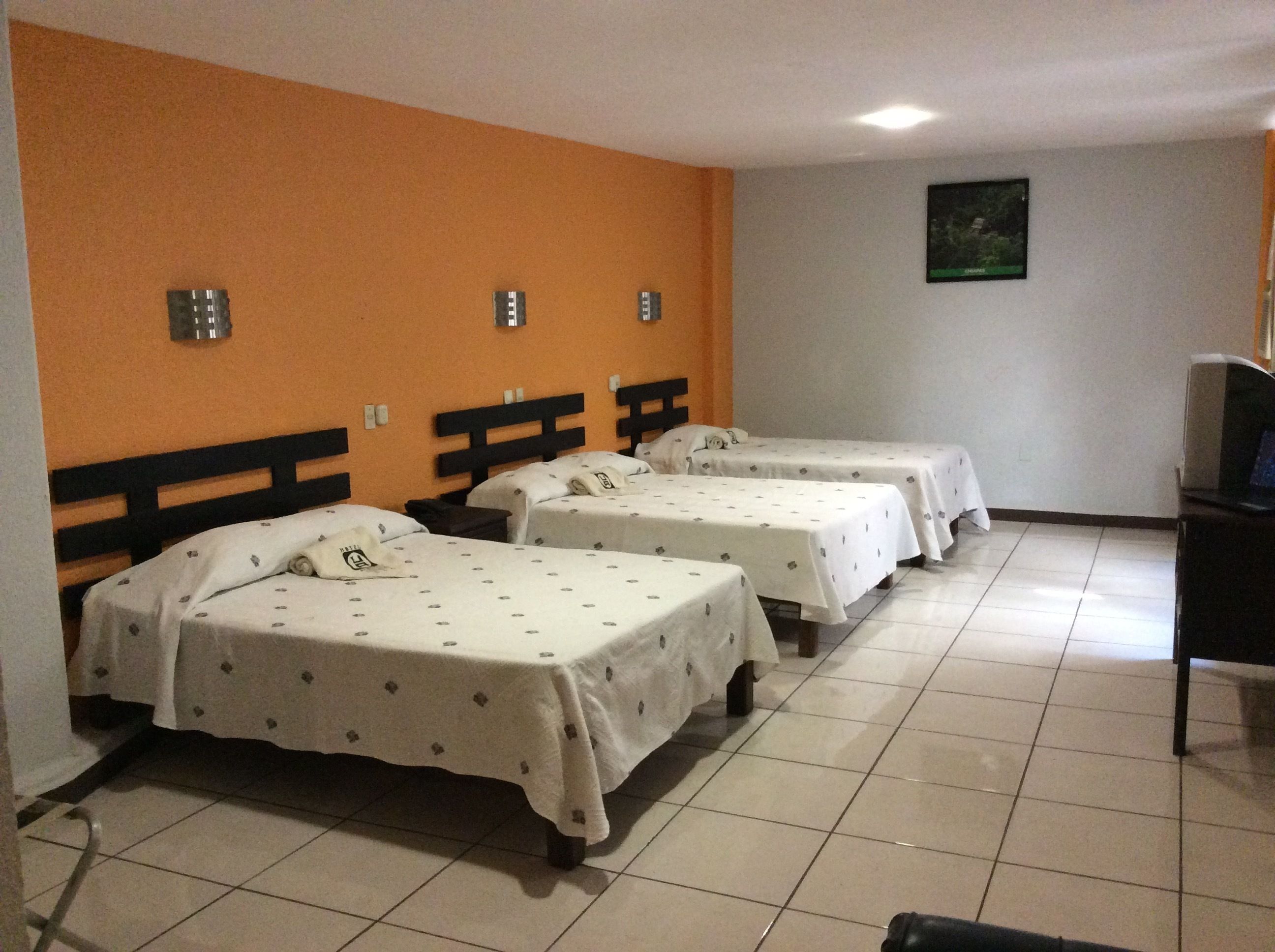Habitación de hotel con tres camas individuales, un televisor y un escritorio pequeño.