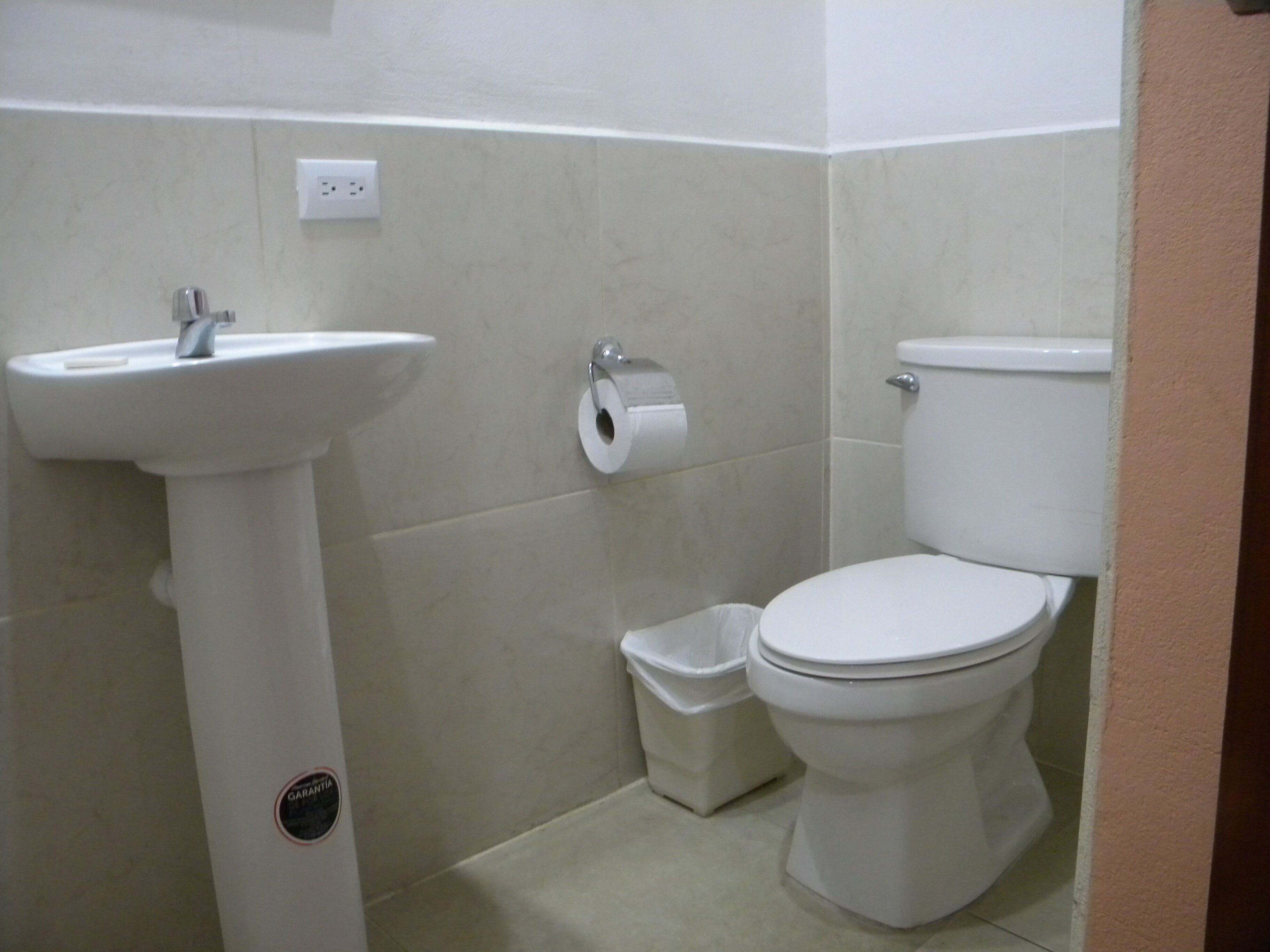 A bathroom with a white sink, toilet, and trash bin.