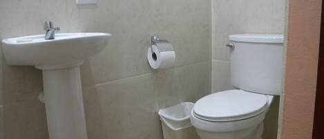 A bathroom with a white sink, toilet, and trash bin.