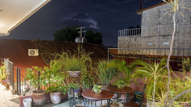 Un patio al aire libre con varias mesas y sillas, rodeado de macetas con plantas y un piso de baldosas.