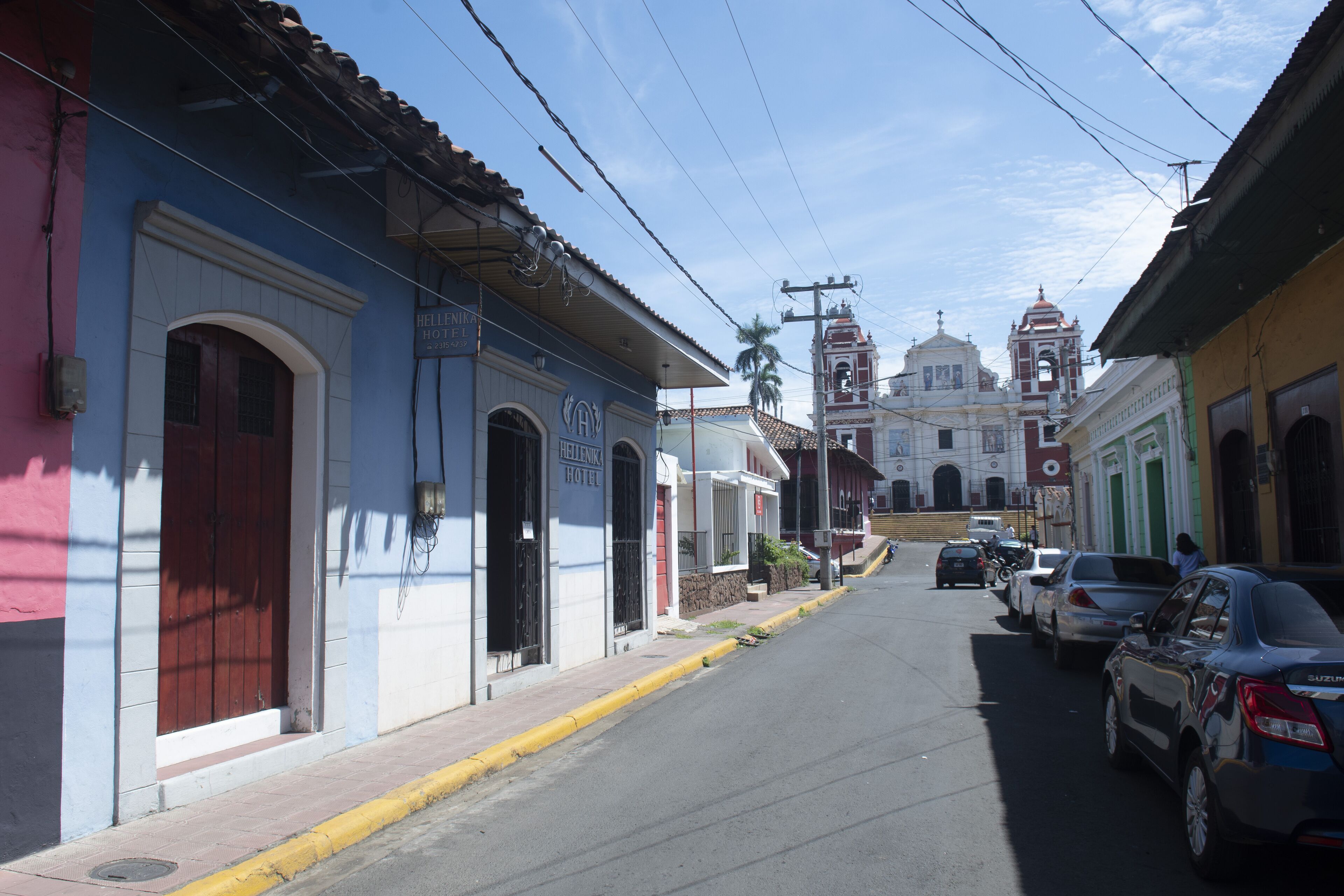 A street view with a hotel named "Hotel Helene" on the left, a church with a bell tower in the background, and parked cars along the street.
