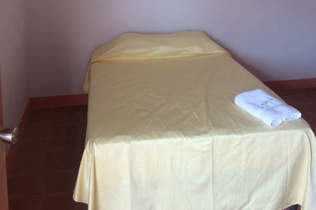 A single bed with a yellow bedspread and a white towel on it.