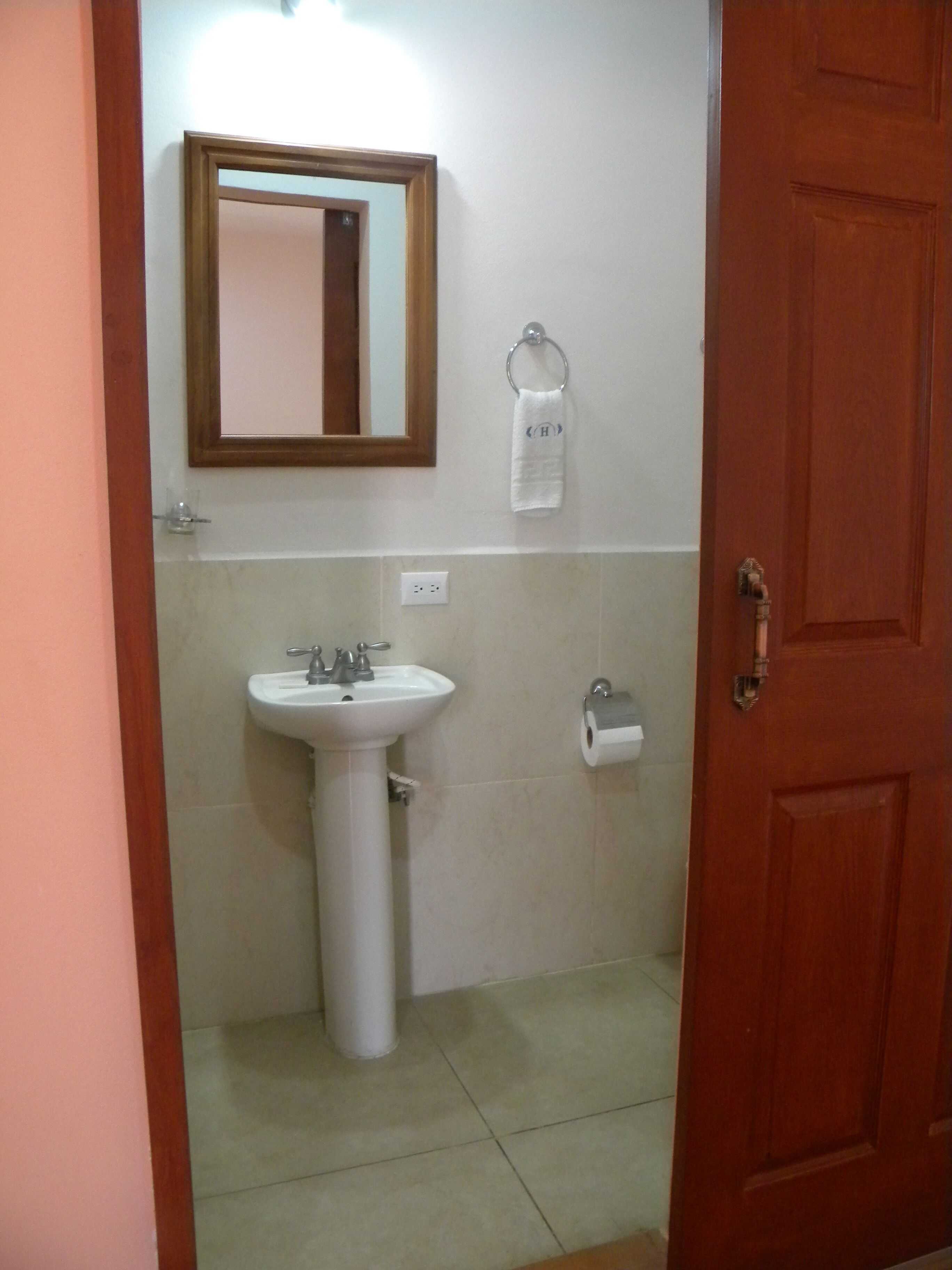 Casa de banho com lavatório, espelho, porta-toalhas e rolo de papel higiénico.