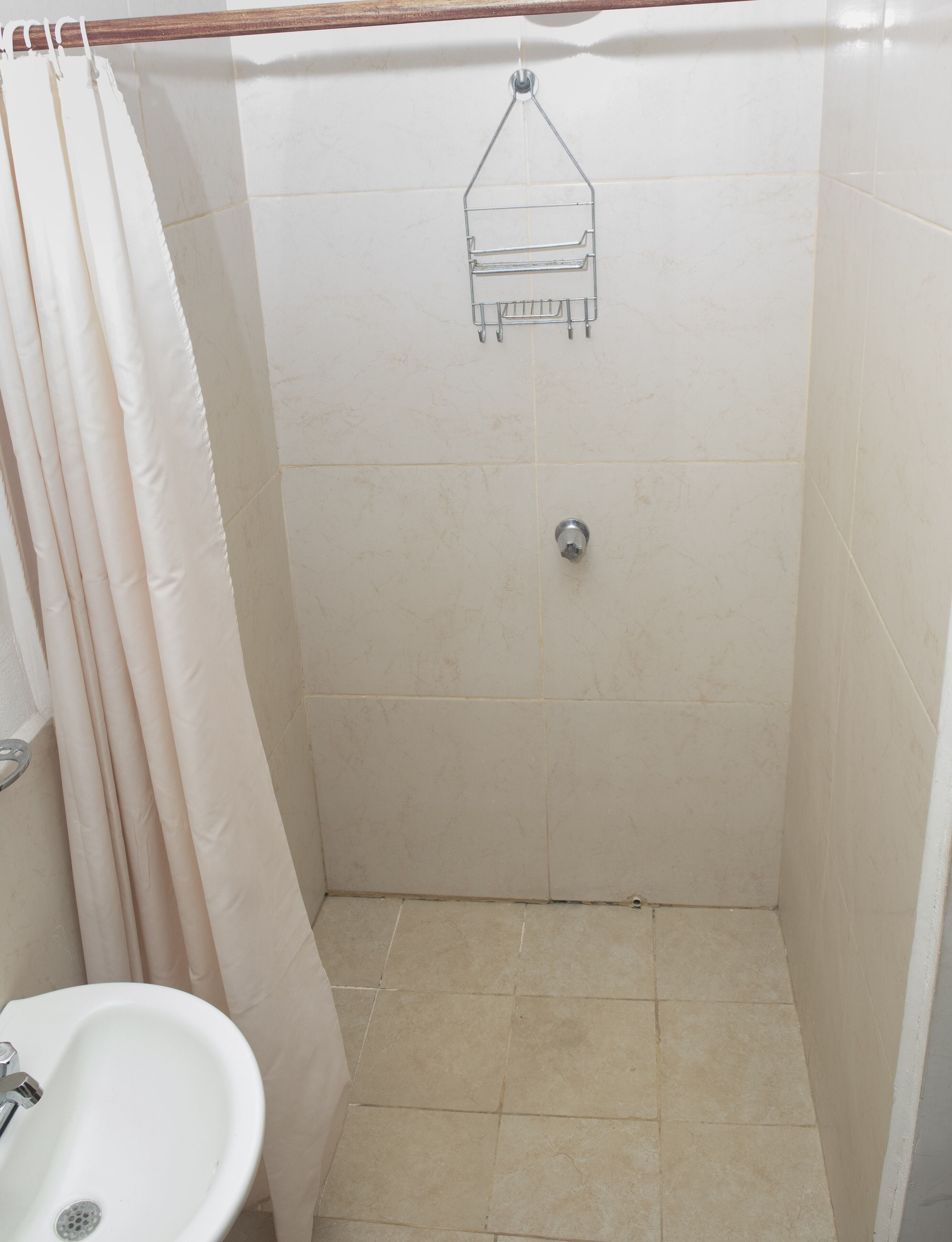 A small, tiled shower stall with a shower curtain, a toilet, and a sink.