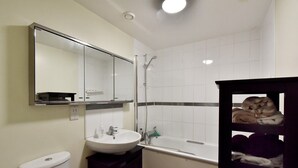 A bathroom with a white sink, mirror, and shower. There is a toilet and a shelf with towels. - Belgravia Apartments- Wilton Road (London)