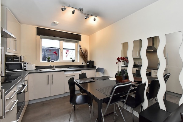A modern kitchen with a dining area, featuring stainless steel appliances, a window with flowers, and a unique wavy mirror design.