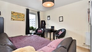 A modern bedroom with a bed, a desk, two chairs, a map on the wall, and a window with curtains. - Belgravia Apartments- Wilton Road (London)