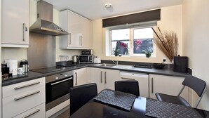 A modern kitchen with stainless steel appliances, a window with a view, and a dining area with a black table and chairs. - Belgravia Apartments- Wilton Road (London)
