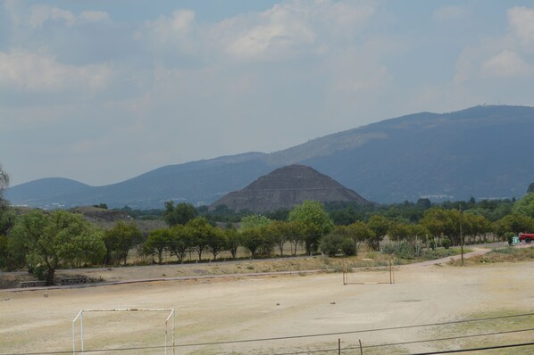 A soccer field with goalposts, surrounded by trees and a hilly landscape in the background.