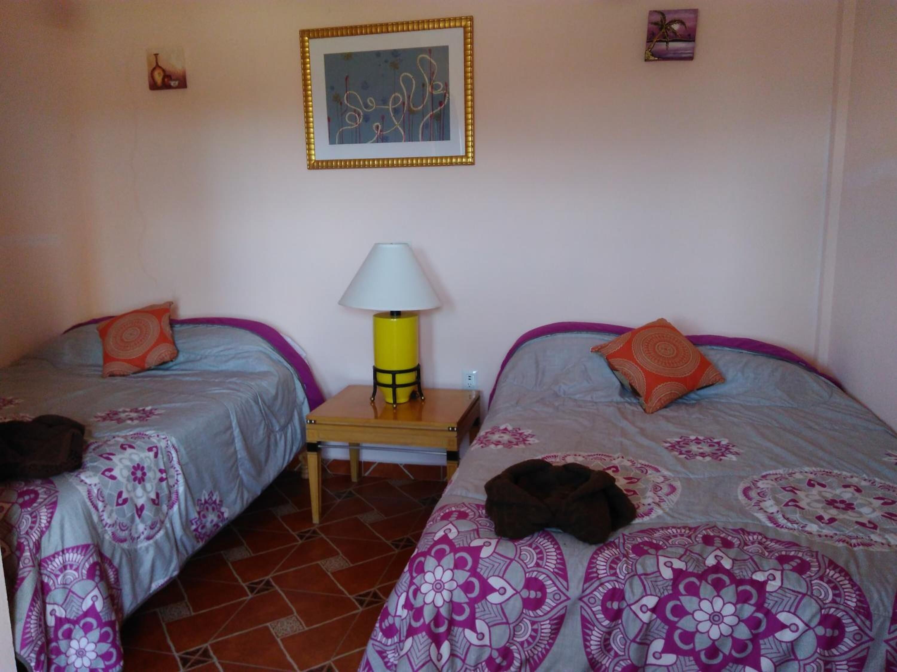 A bedroom with two beds, a nightstand, a lamp, and a framed picture on the wall.