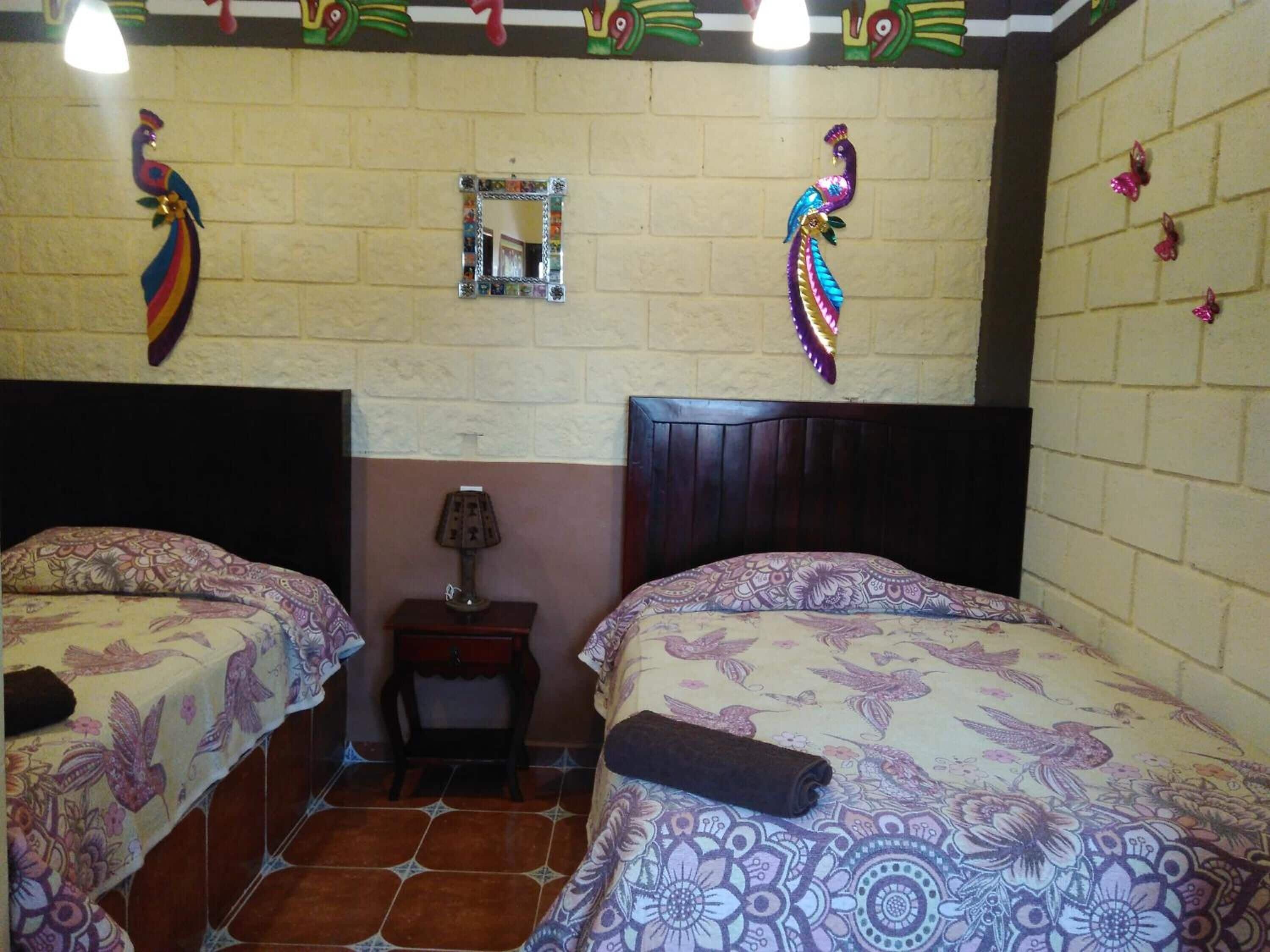 Une chambre avec deux lits, une petite table avec une lampe et des œuvres d’art décoratives au mur.