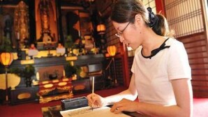 A person writing at a table in a room with traditional decor, including a shrine and hanging lanterns. - Daienin (Koya)