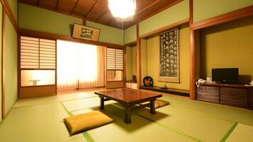 A traditional Japanese room with tatami flooring, a low wooden table, sliding doors, and a television on a wooden cabinet.