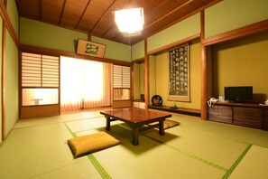 Une pièce de style japonais traditionnel, avec un sol recouvert de tatamis, une basse table en bois, des portes coulissantes et un téléviseur posé sur un meuble en bois.