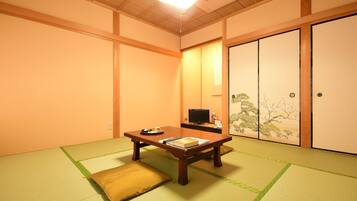 A traditional Japanese room with tatami flooring, a low wooden table, a television, and sliding doors with a nature-themed design.