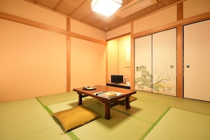 Una habitación japonesa tradicional con suelo de tatami, una mesa de madera baja, un televisor y puertas correderas con motivos naturales.
