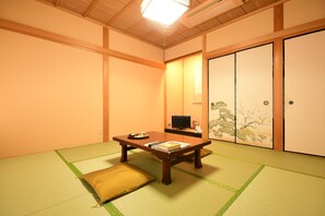 Une pièce de style japonais traditionnel, avec un sol recouvert de tatamis, une basse table en bois, un téléviseur et des portes coulissantes ornées de motifs inspirés de la nature.