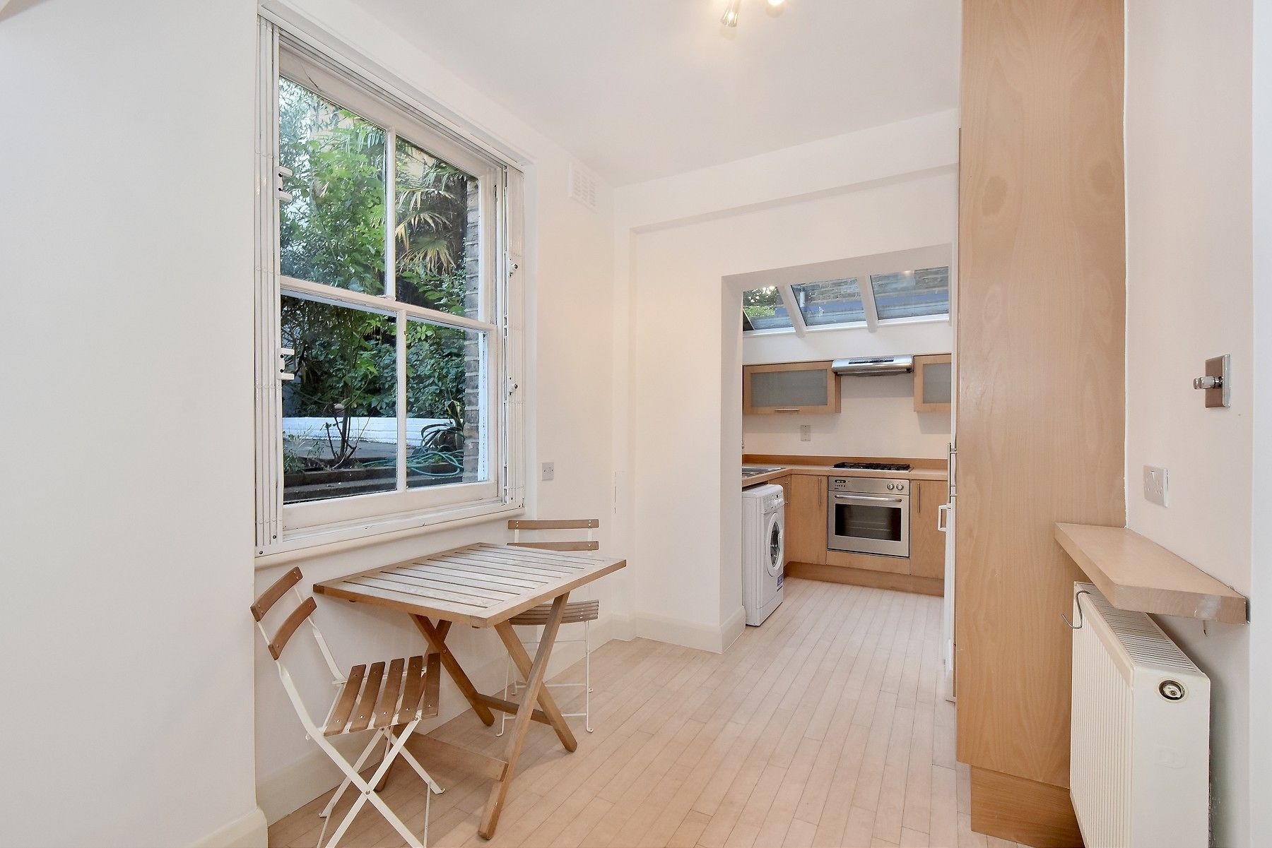 A compact kitchen with a built-in oven, a washing machine, and a window overlooking greenery.