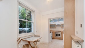 A compact kitchen with a built-in oven, a washing machine, and a window overlooking greenery. - Belgravia Apartments - Cathcart Road (London)