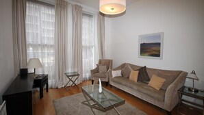 A living room with a sofa, a glass coffee table, a lamp, and a painting on the wall. - Belgravia Apartments - Gloucester Road (London)